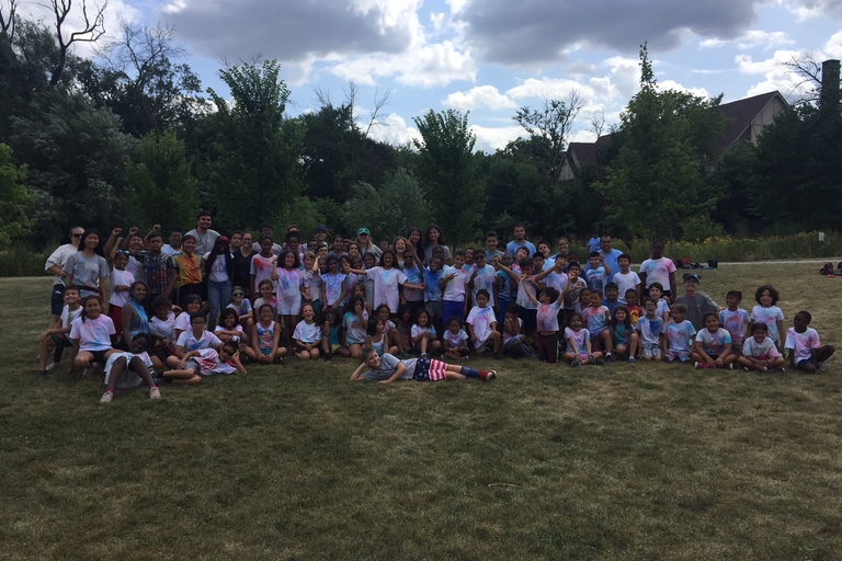Large group of tie-dye-clad children and adults pose for a photo on a grassy field.