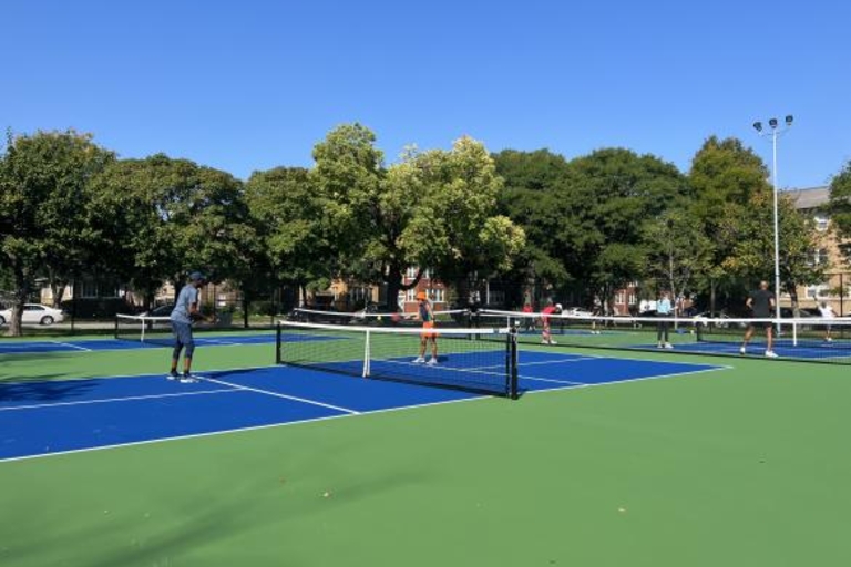 People playing pickleball on blue and green courts on a sunny day.