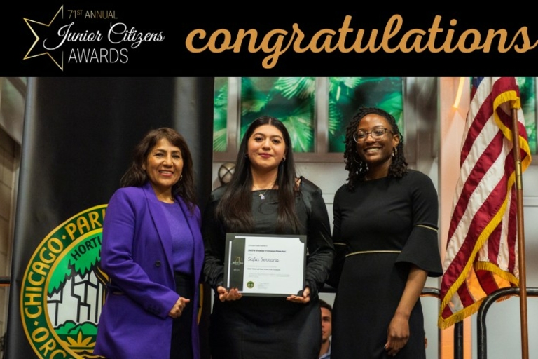Three women pose at an awards ceremony, one holding a certificate. An American flag and Chicago Park District banner are visible.