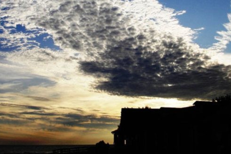 Silhouetted beach house under a dramatic sky at sunset.