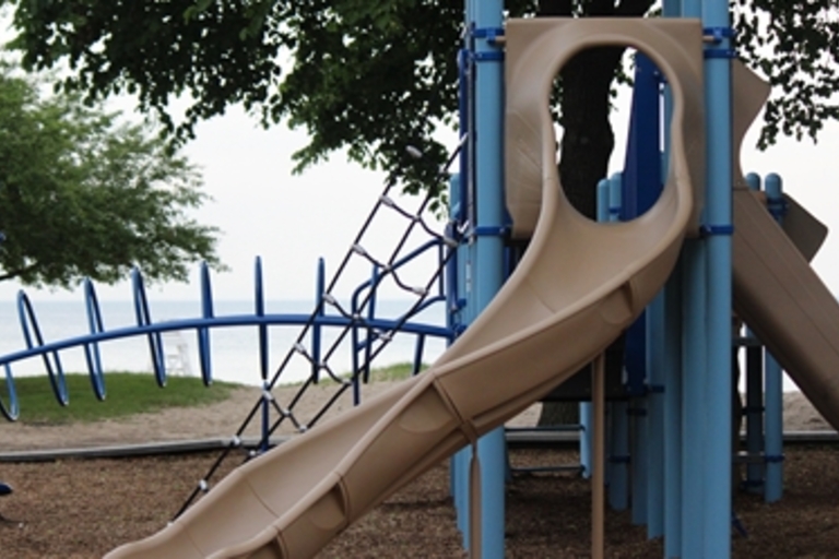 Tan playground slide and blue climbing structure at a beachside park.