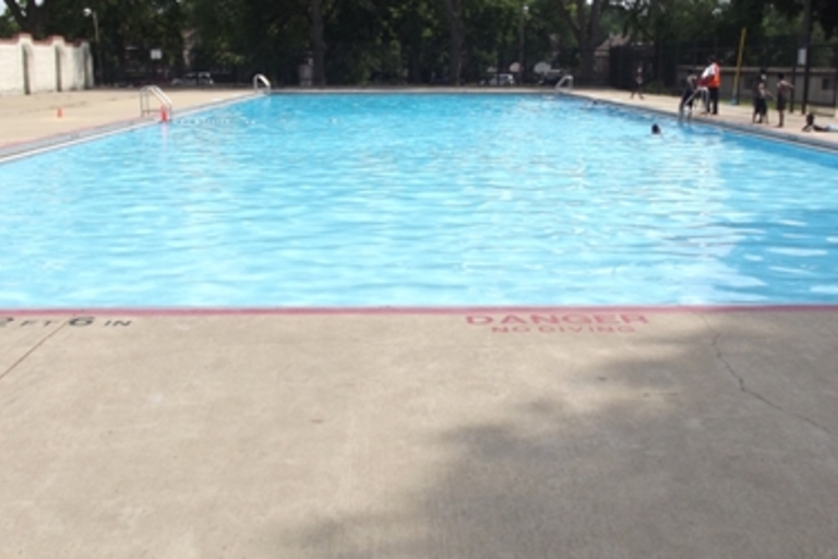 Outdoor community pool with people swimming on a sunny day.