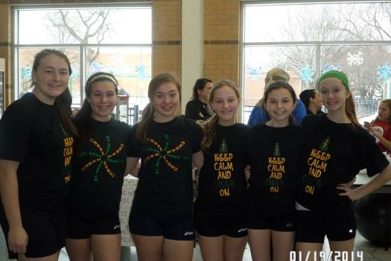 Six girls in matching cheerleading shirts smile for a photo.
