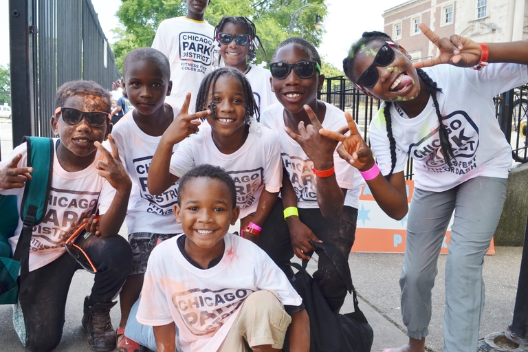 Group of children wearing Chicago Park District shirts, smiling and making hand gestures.
