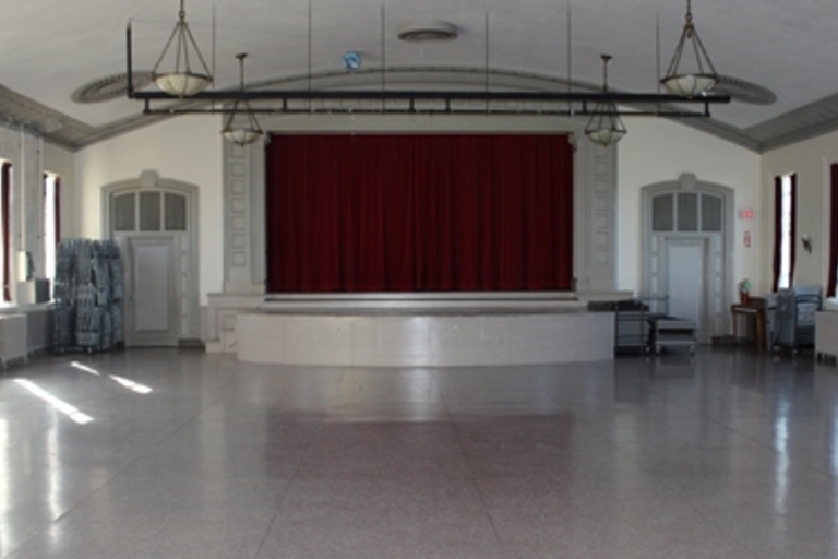 Empty auditorium with maroon stage curtain and gray floor.
