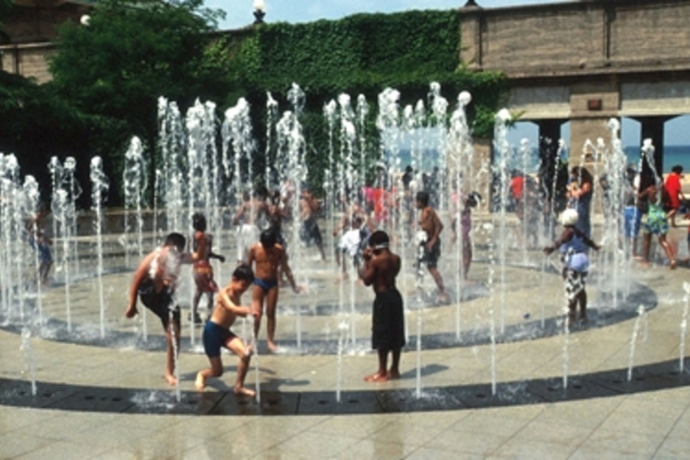 Children play in a splash pad fountain on a hot day.
