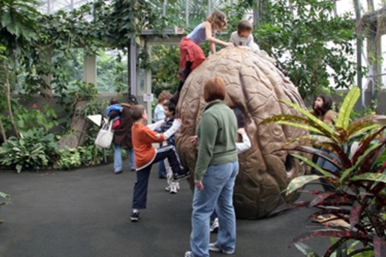 Kids climb a giant seed sculpture in an indoor botanical garden.

