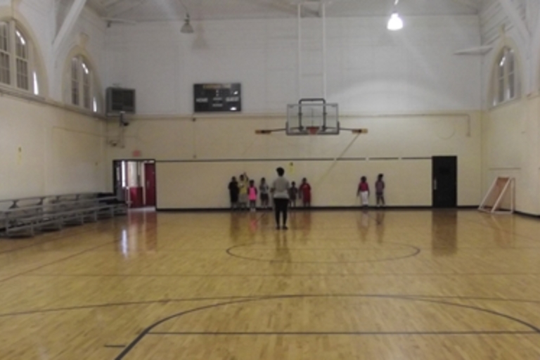 Children line up against the wall in a school gymnasium.