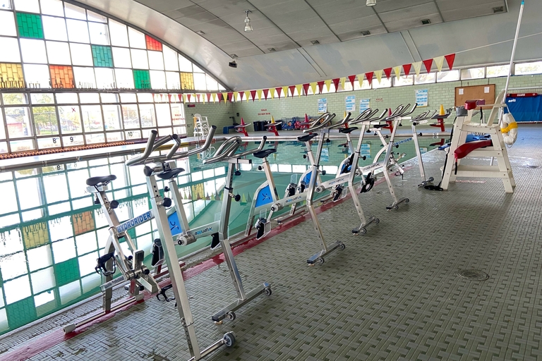 Stationary bikes for aquatic exercise are lined up on the edge of an indoor pool.