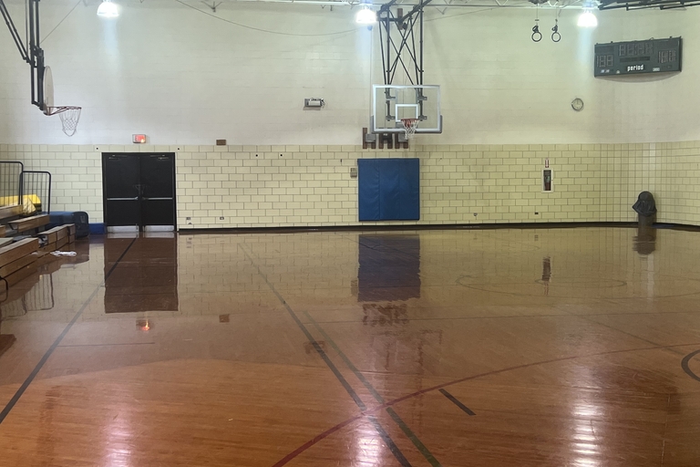 Empty gymnasium with polished wooden floor and basketball hoop.