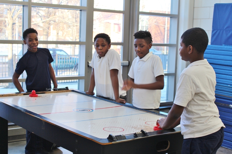 Four boys play air hockey indoors.