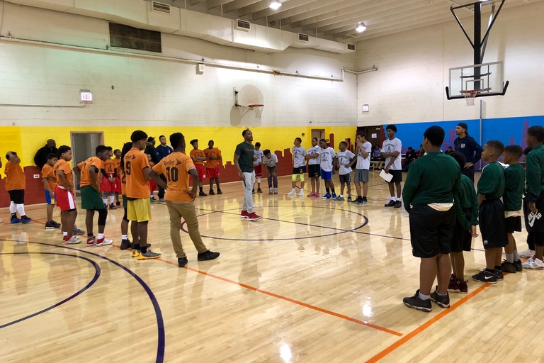 Youth basketball team gathers at center court as a coach addresses them.
