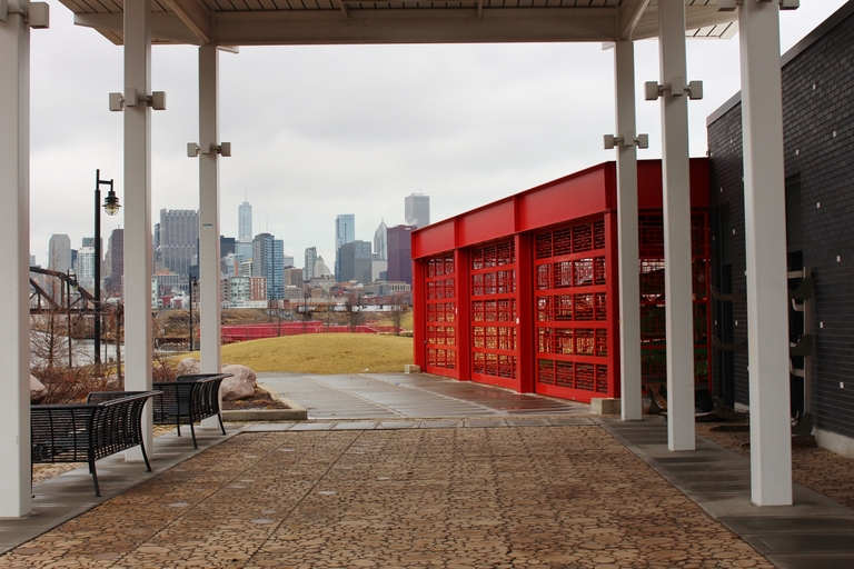 Red gate with geometric design, benches, and Chicago skyline in background.