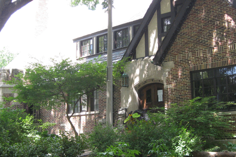 Brick Tudor house with shrubs and small trees in front.