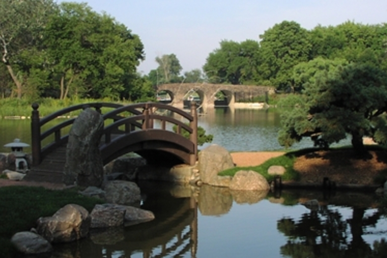 Wooden footbridge in a serene Japanese garden with a stone bridge in the background.
