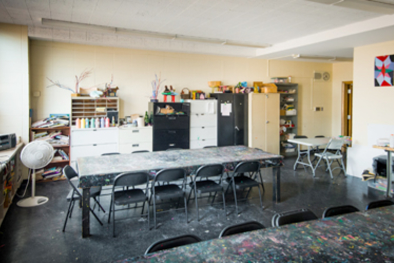 Messy art studio with paint-splattered tables and various art supplies.