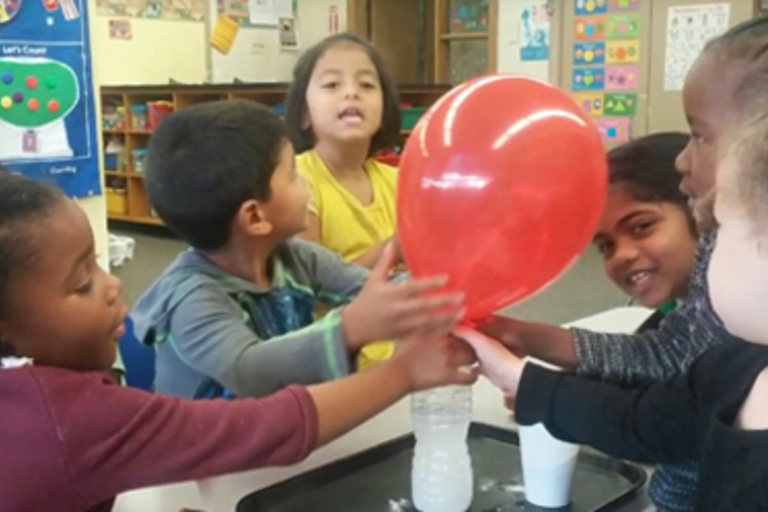 Children conduct a science experiment with a balloon.
