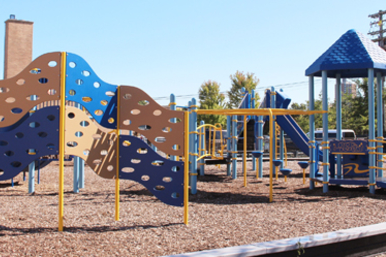Blue and gold playground with climbing structures and a slide. Wood chip ground cover.