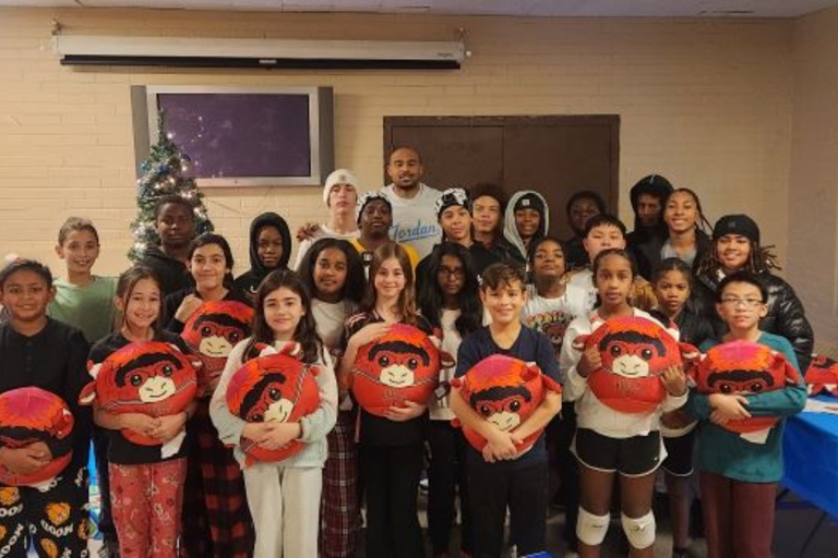 Group photo of children and adults holding monkey plushies, with holiday decorations and a table of gifts in the background.