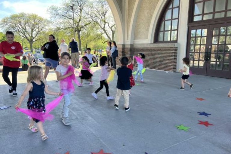 Children dance with colorful scarves outside a building.