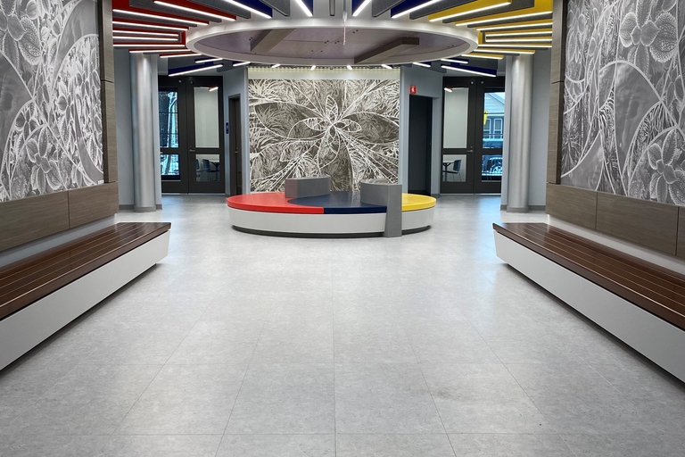 Modern hallway with colorful overhead lighting and floral wall art. Circular seating area in center.