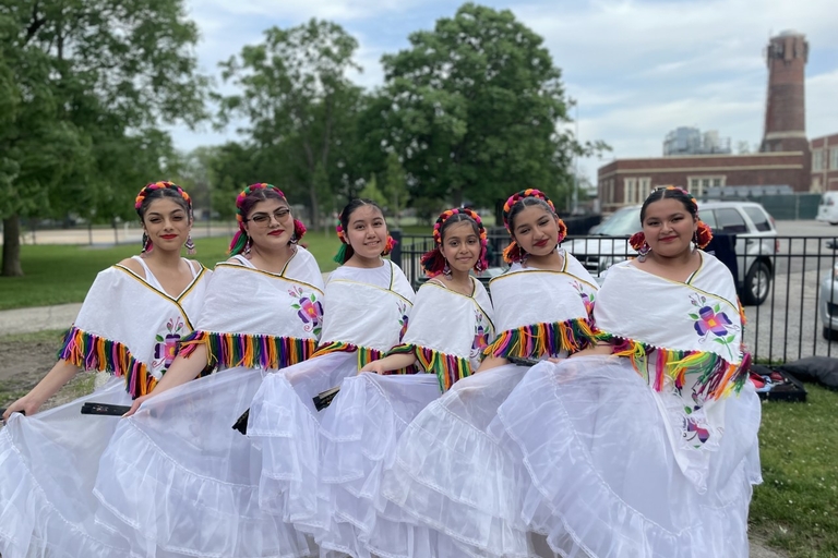 Five dancers in white skirts and colorful shawls smile for a photo.
