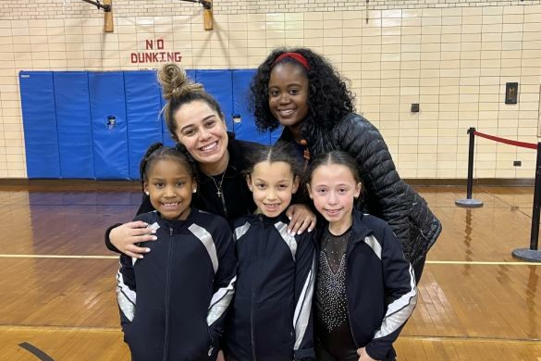 Four young gymnasts and their coach pose for a photo in a gymnasium.
