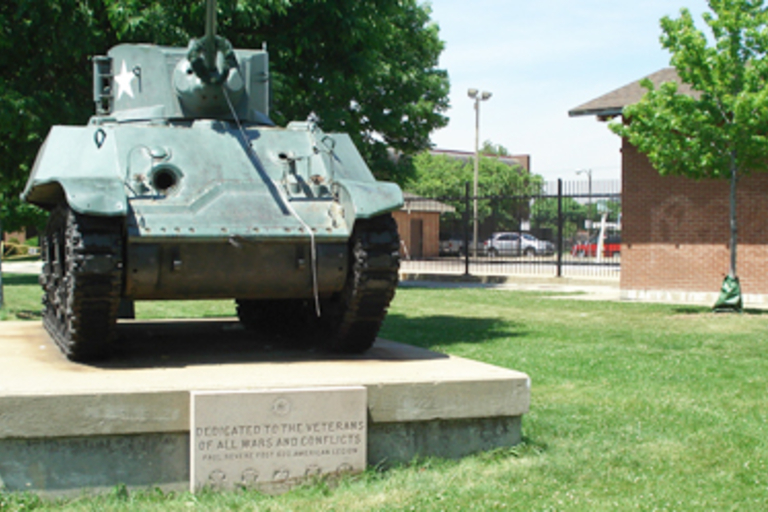 Green WWII-era tank on concrete pedestal in park.