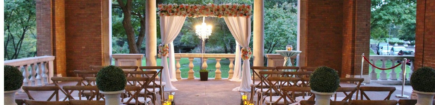 Outdoor wedding venue decorated with floral arch and wooden chairs.