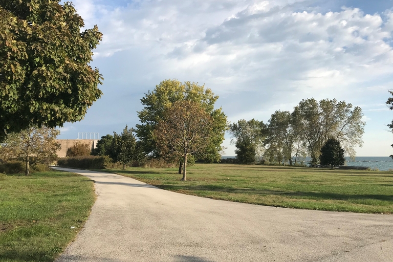 Paved path curves through grassy park with trees and a view of Lake Michigan.