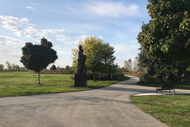 Paved path winds through a park with a statue and a bench.