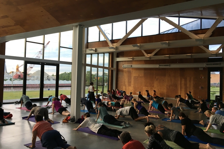 Large group performs a yoga pose in a spacious room with large windows.