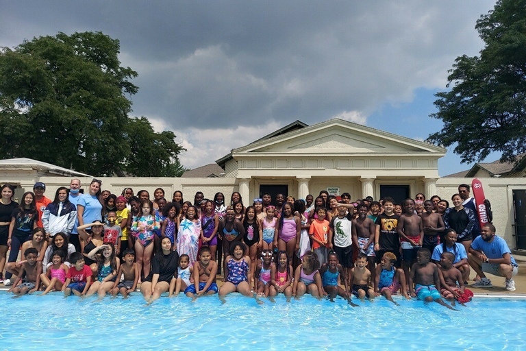 Large group of children and adults pose at the edge of a swimming pool.