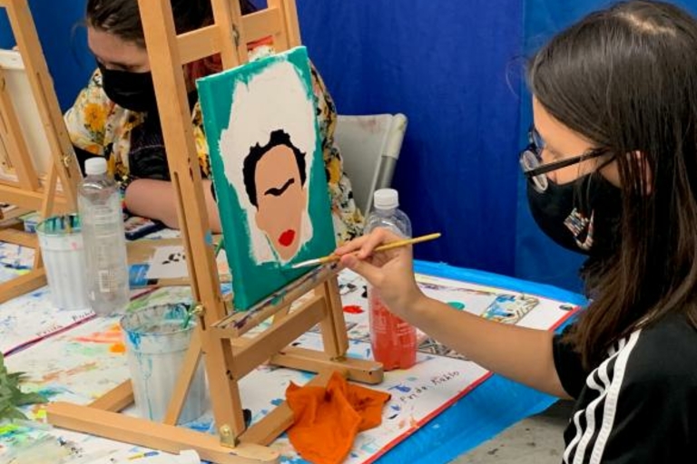 Girl painting a portrait of Frida Kahlo on a small canvas.