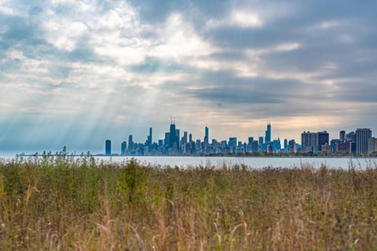 Chicago skyline across lake with sunbeams and cloudy sky.