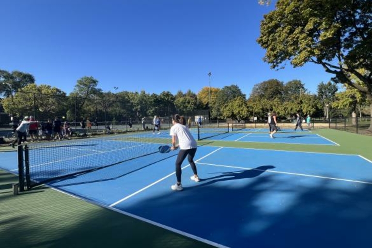 People playing pickleball on blue courts in a park.