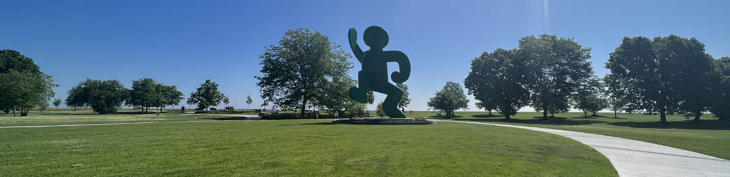 Large green abstract human-like sculpture in a park setting.