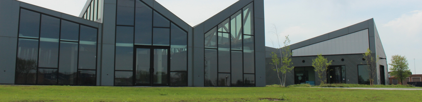 Modern building with angled glass walls and a grassy lawn.