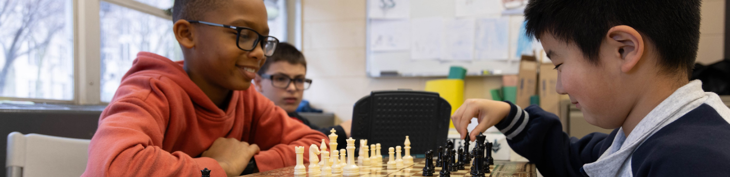 Two children play chess, another child watches.
