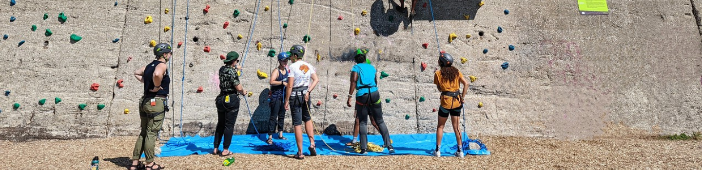 Group of young rock climbers preparing at the base of a climbing wall.