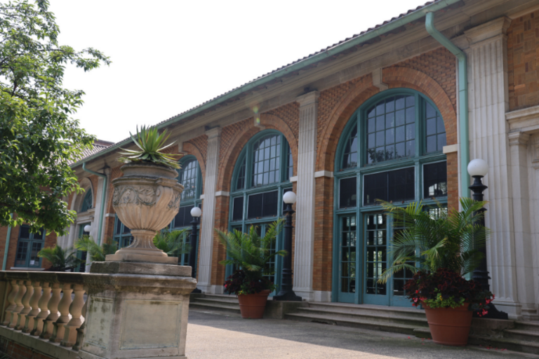 Brick building with arched, teal-framed windows and potted plants.