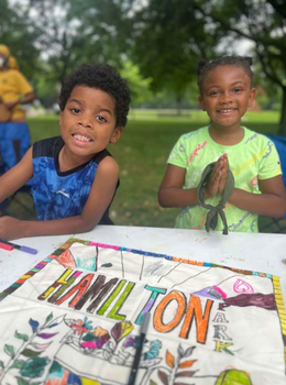 Two smiling children at a table with a Hamilton Park banner they decorated.