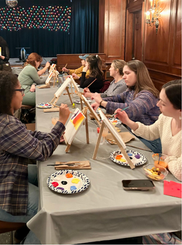 Group of people painting on small canvases at a long table.
