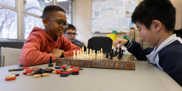 Two boys playing chess in a classroom.