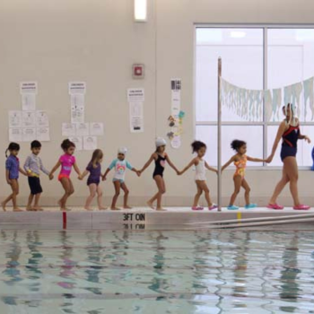 Swim instructor leads children poolside.