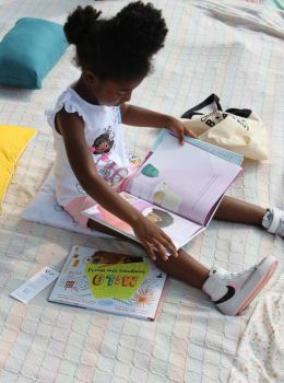 Young girl sitting on a blanket reading a children's book.