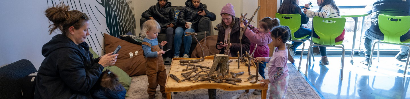 Children and adults play with sticks at a nature-themed table.