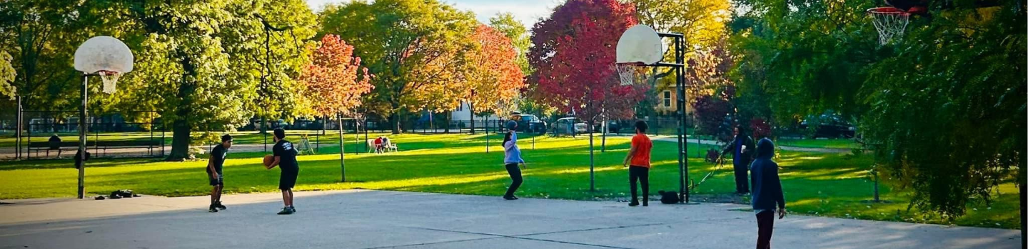 People playing basketball on a court in a park with fall foliage.