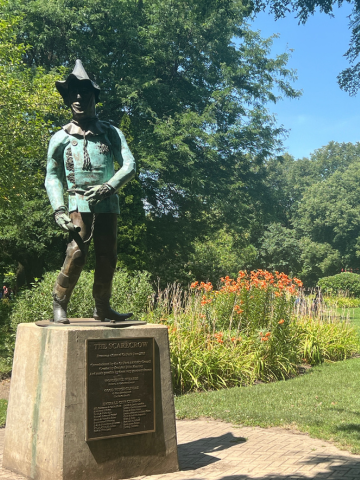 Bronze statue of the Scarecrow from the Wizard of Oz in a park setting.
