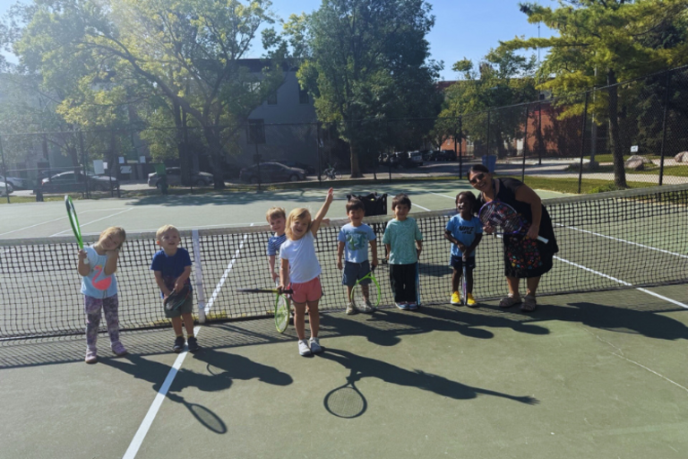 A tennis coach and children on a court.